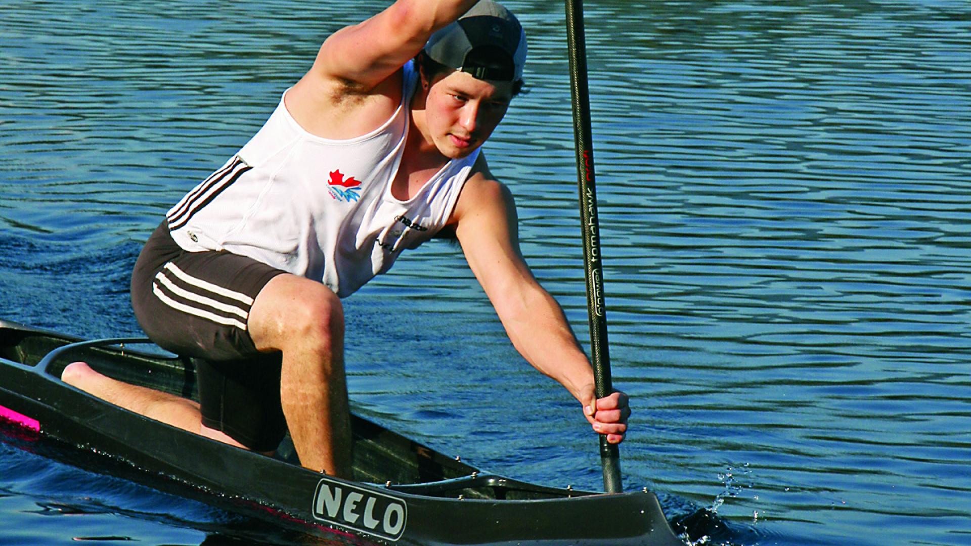 Sean McBeath kneels to paddle across a lake on his paddleboard.