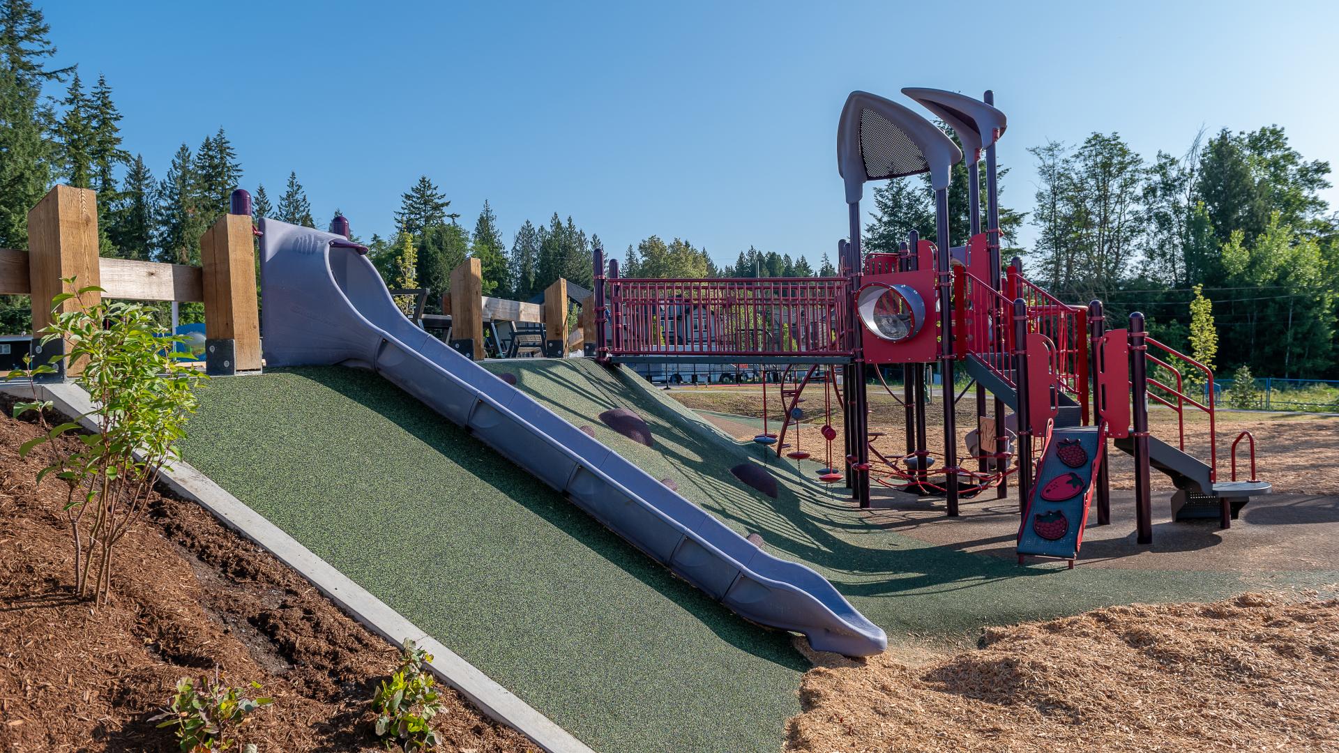 A hill slide on a green rubber hill with red play structure in background