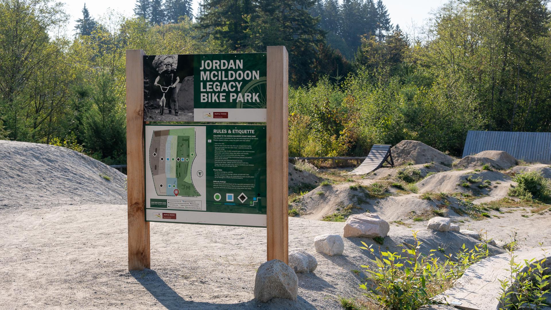 Jordan McIldoon Legacy Bike Park entrance sign with dirt bike park in the background