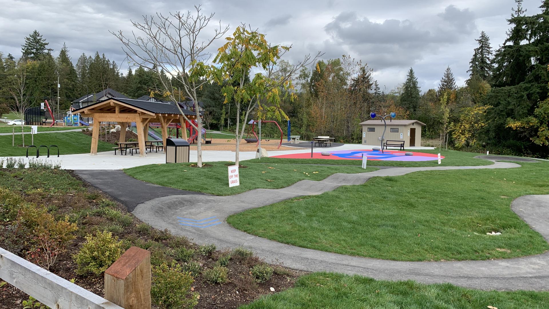 An asphalt bump track through grass lawn with picnic shelter and washroom in background