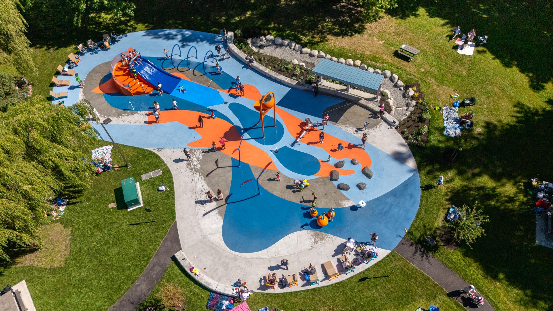 An aerial image of the new spray park, with a fish graphic painted on the concrete deck and many children playing