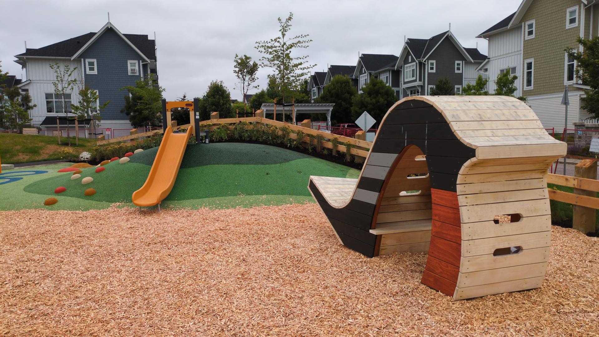 A junior playground including yellow hill slide on green rubber hill, and a wood bird-shaped play hut. 