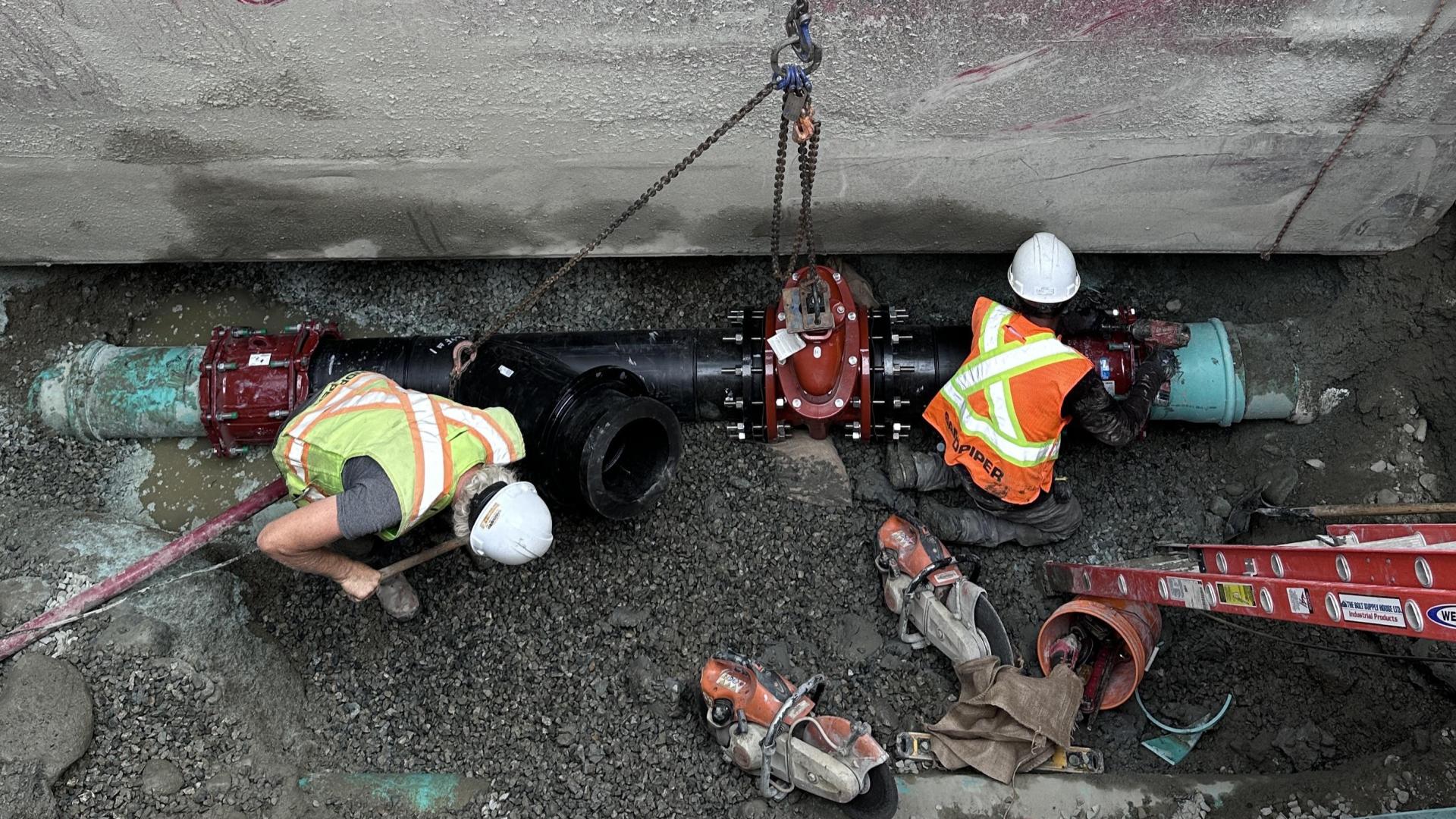 Workers in a trench install a valve on a water pipe