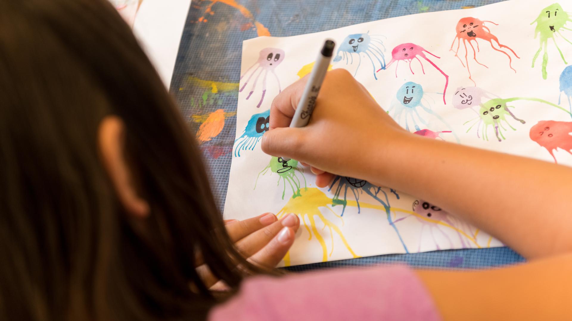 A young girl puts faces on paint splatters in black ink.