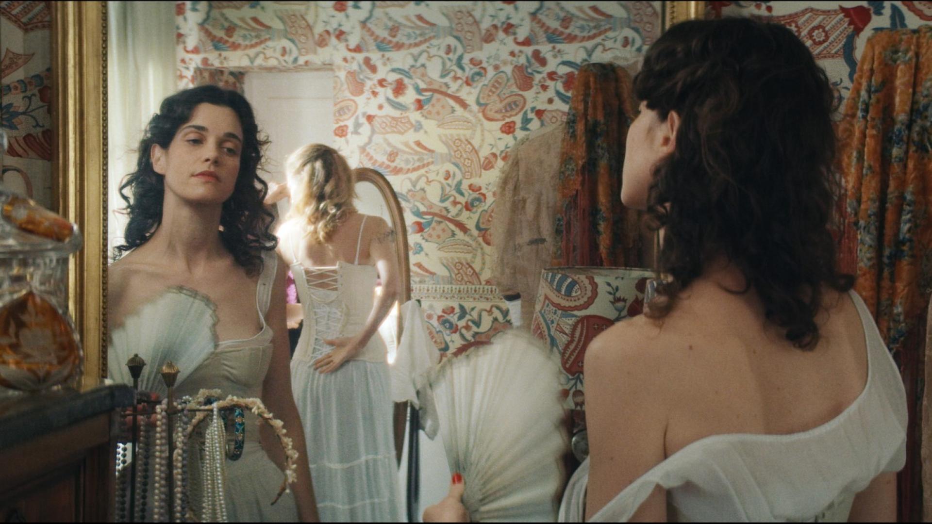 A woman wearing a white ballgown looks at herself in the mirror.