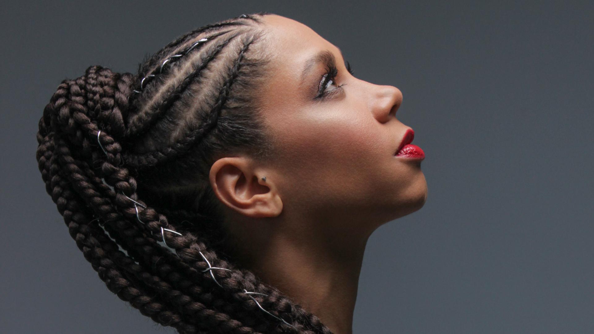 Tina Leon, wearing thick braids looks up towards the light against a striking grey background.