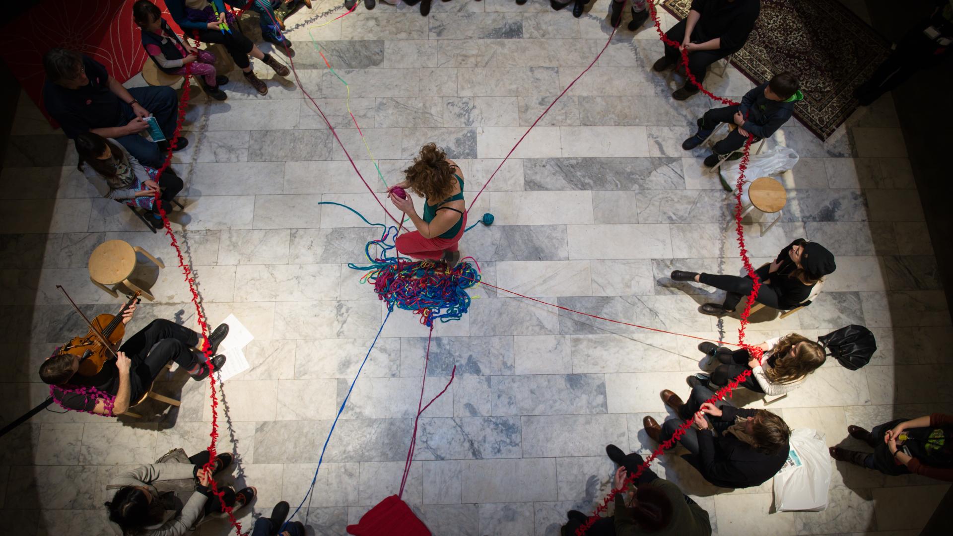 Circle of people holding pieces of yarn