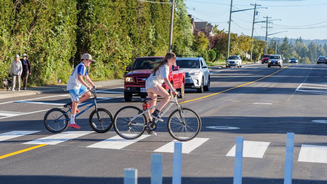 Two children on bicycles cross at a crosswalk