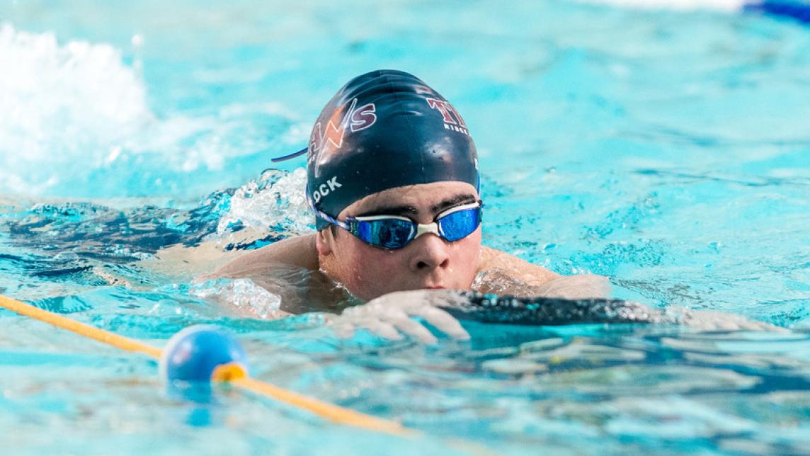 A boy wearing a swim cap and googles kicks down a designated swim lane at a pool.