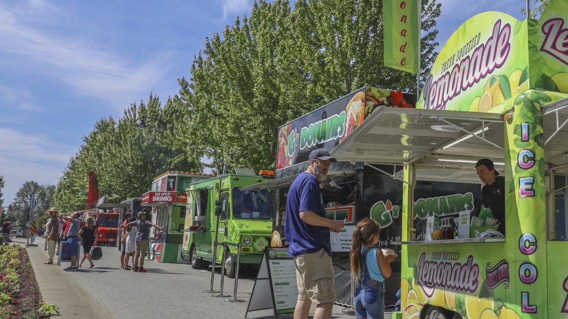 A line of food trucks rest alongside a street, catering to passersby.