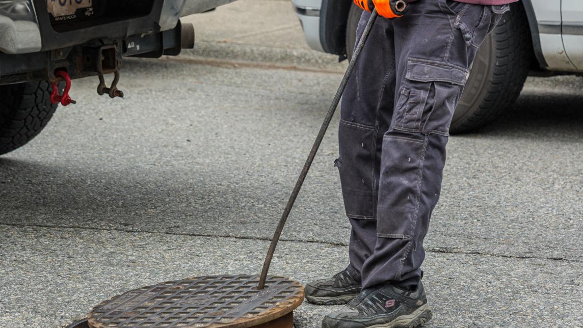 A worker uses a tool to pull off a maintenance hole cover