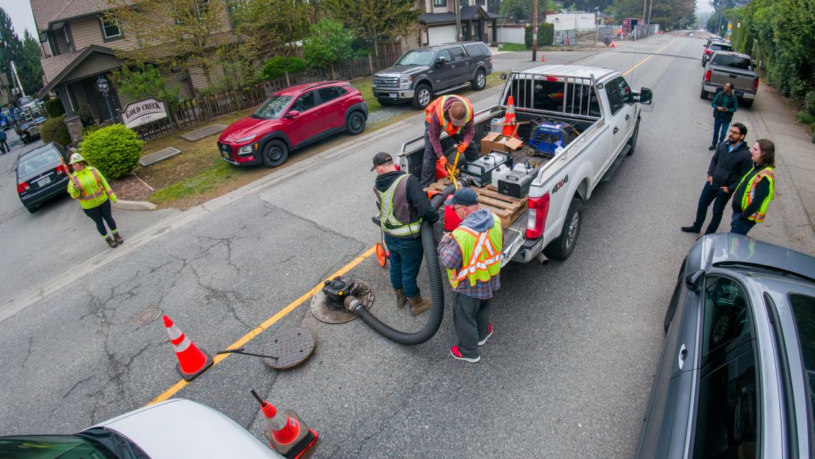 Crews connect fog testing equipment to a maintenance hole from the back of a pickup truck