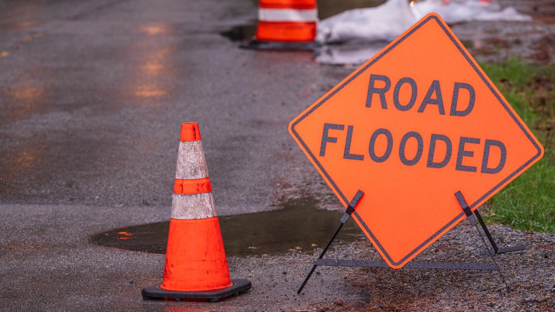 A road flooded sign and traffic cone on a roadway