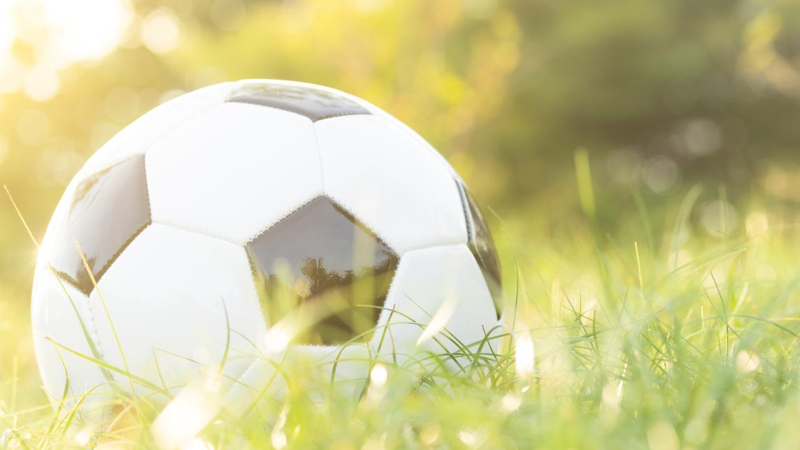 A soccer ball sits in a grassy field on a sunny day.