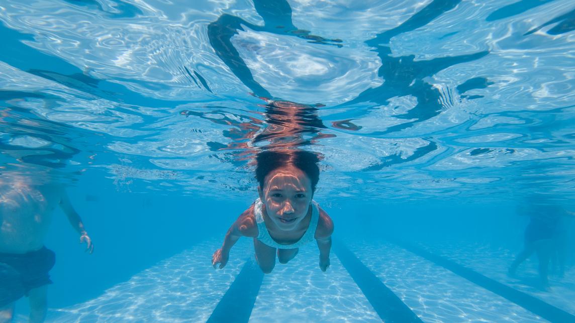 An underwater view of a girl swimming in a pool, just below the surface.
