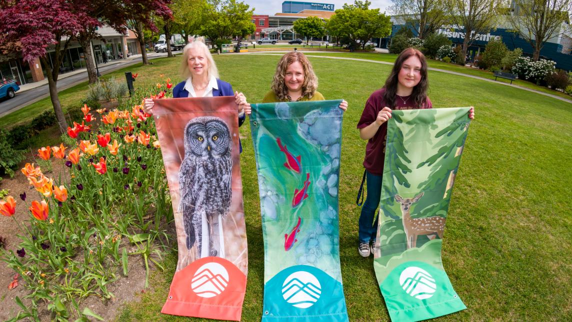 The three artists behind the winning 2026 Banner designs stand in Memorial Peace Park with the completed banners.