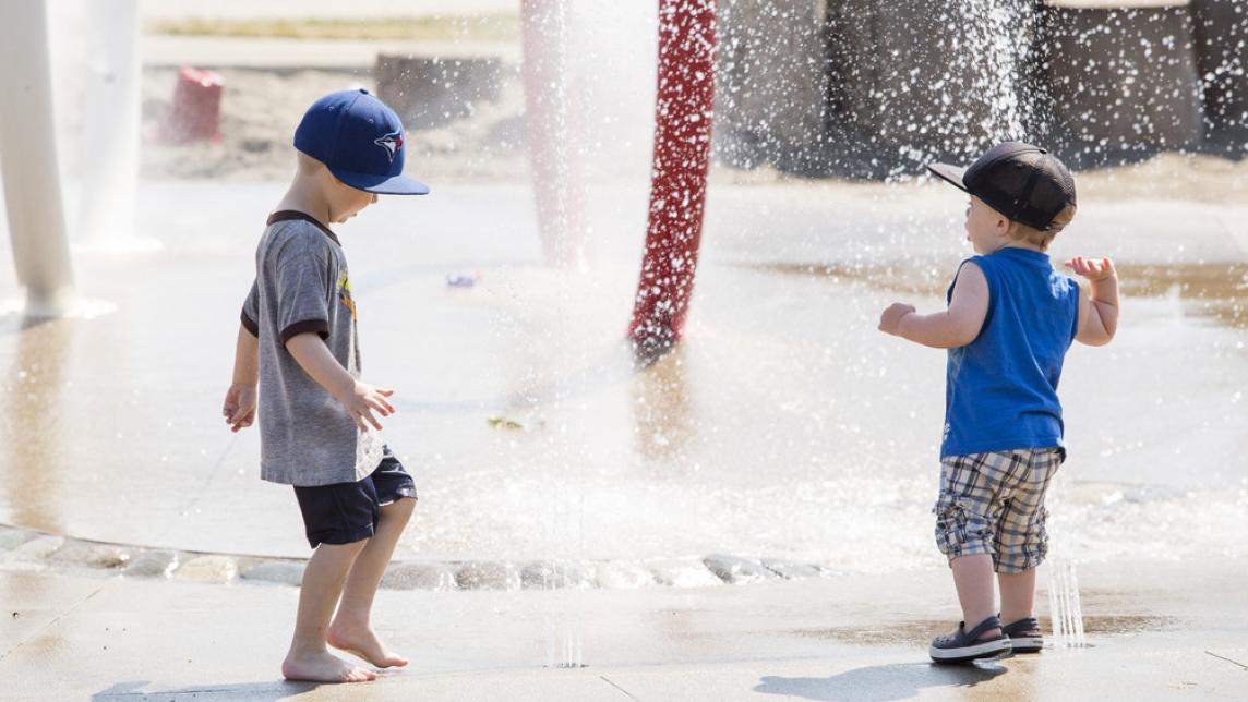 two children in ball caps enjoying a spray park in the sun