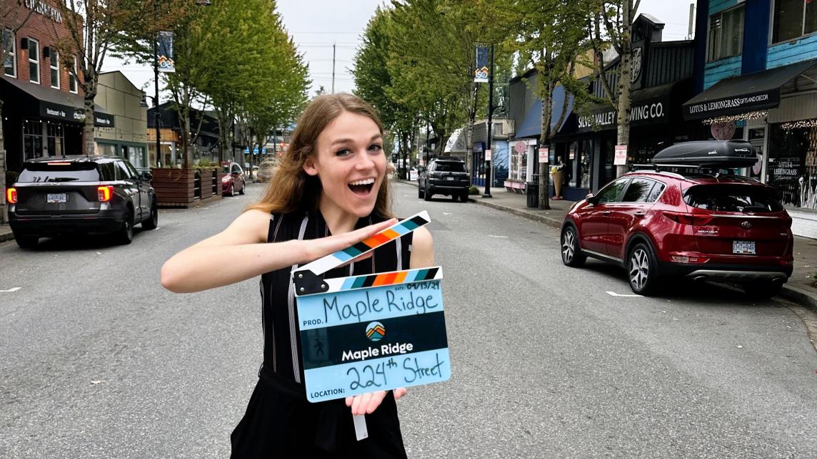 A person holding a Maple Ridge-branded film slate on 224 Street.
