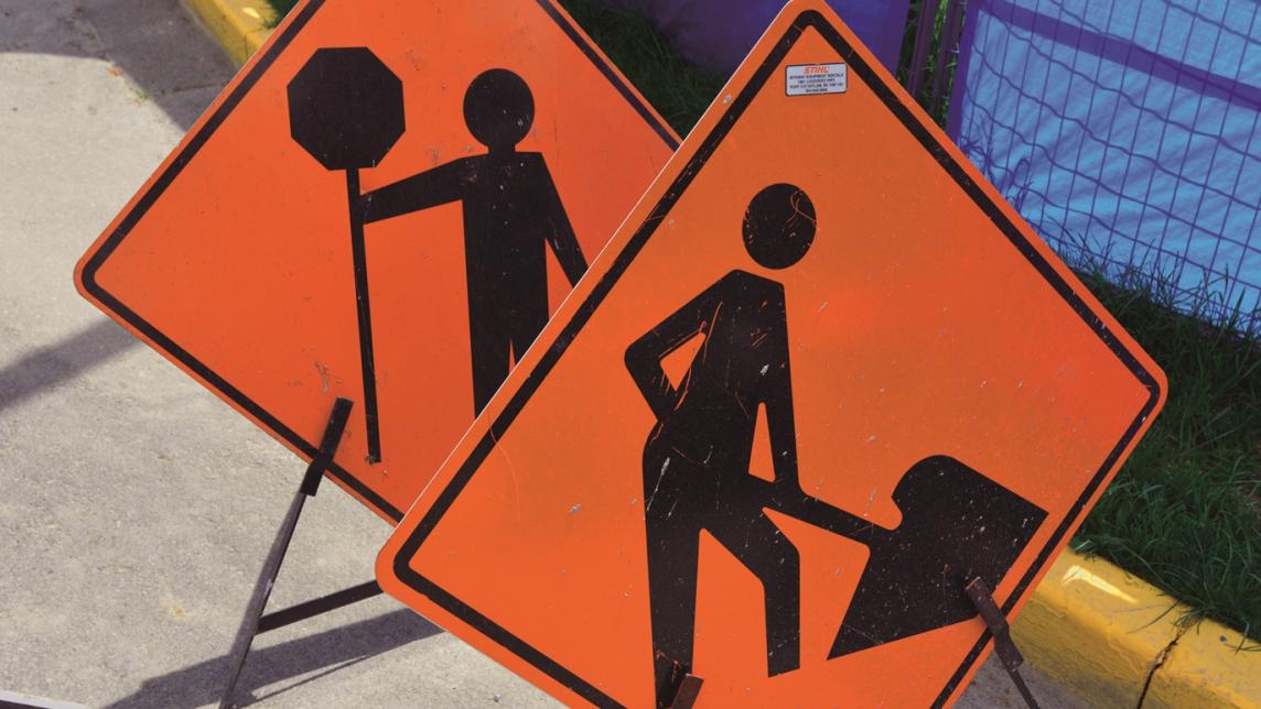 Two construction signs, one showing a flagger one showing a worker digging