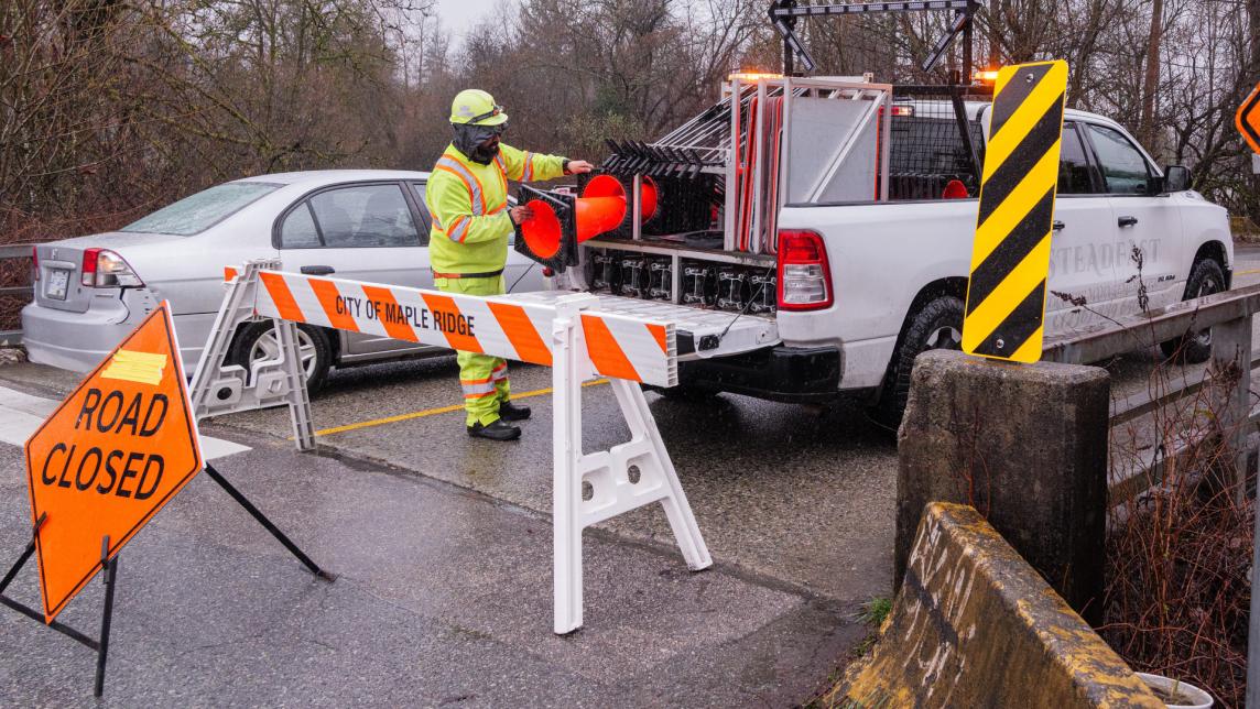A city worker gets some orange pylons down from his truck to block off a bridge.