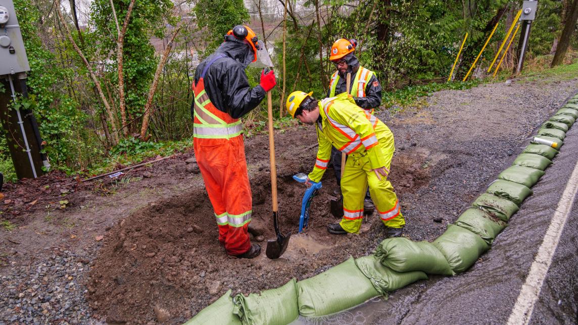 Operations workers digging hole and using sandbags for flood prevention along road. 