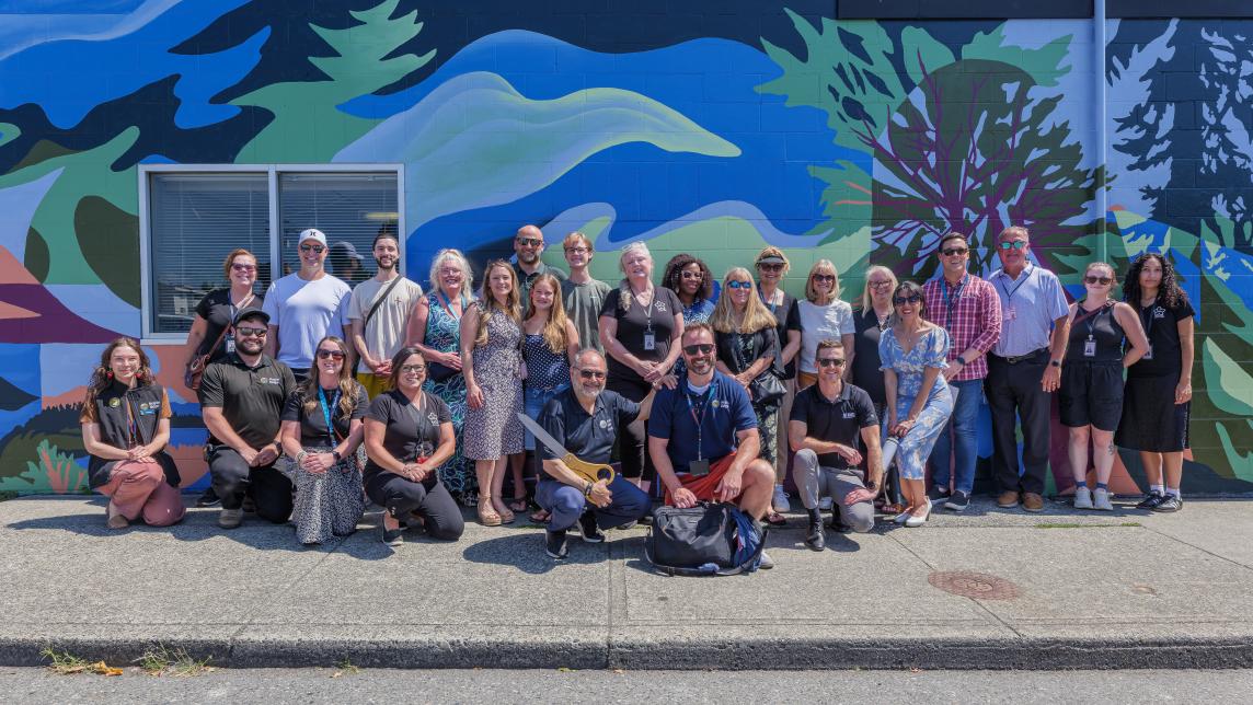 The crowd in attendance stands up against the mural for a picture.