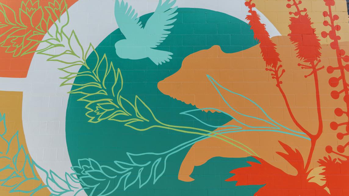 A close up of the mural depicting a bear silhouetted by the moon with an owl flying above it and abstract plants in the foreground.
