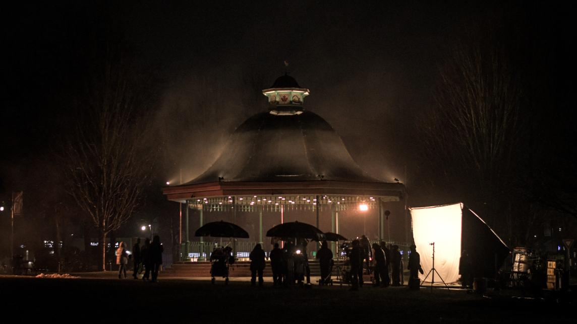 A behind the scenes photo of The Tipline Murders filming in front of the bandstand in Memorial Peace Park