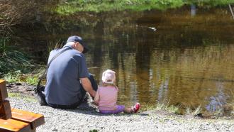Older man sitting with young girl beside river