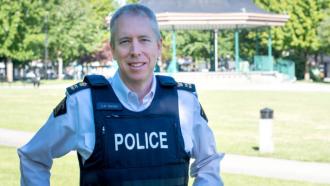 Adam Gander stands in front of the bandstand at Memorial Peace Park, smiling in his police uniform.