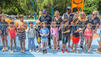 Mayor Dan Ruimy, MLA Lisa Beare, and Maple Ridge Councillors Judy Dueck, Korleen Carreras and Onyeka Dozie stand behind a line of kids, ready to cut the ribbon and officially open the Maple Ridge spray park.