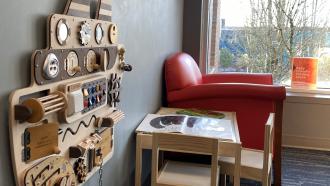 A smooth red armchair sits next to the window, with a child-sized table and chairs and wall-mounted wooden play apparatus beside it.
