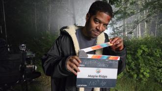 An actor with stage makeup that make it look like his head is bleeding holds a Maple Ridge-branded film clapper that reads July 18, 2026, Prod. Pathetic Fallacy, Location, 130th Ave.