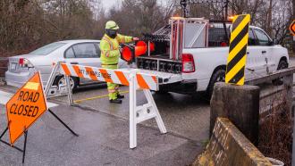 A city worker gets some orange pylons down from his truck to block off a bridge.