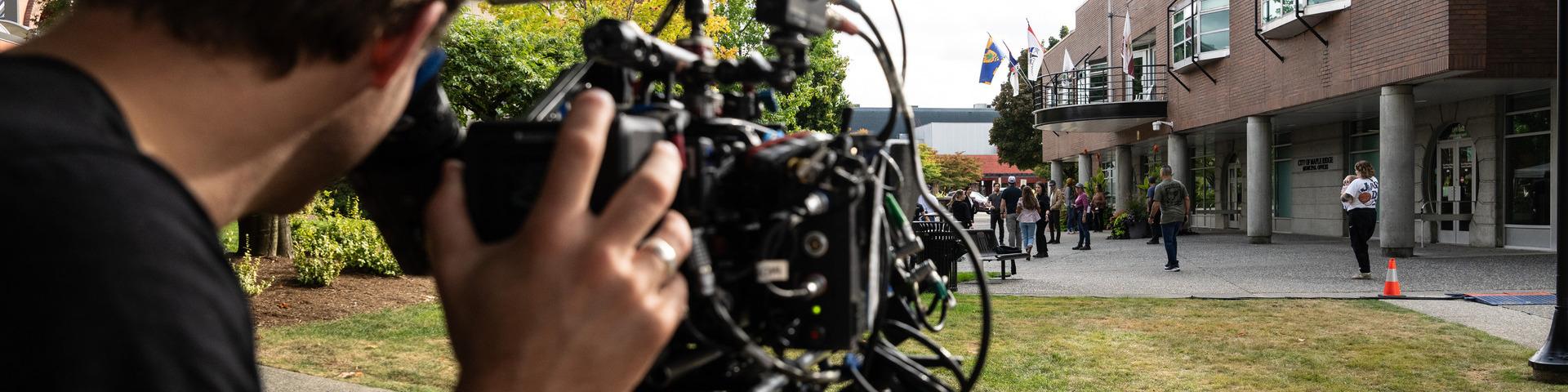 A man uses a professional film camera to film a wide shot in front of the Maple Ridge Municipal Hall.