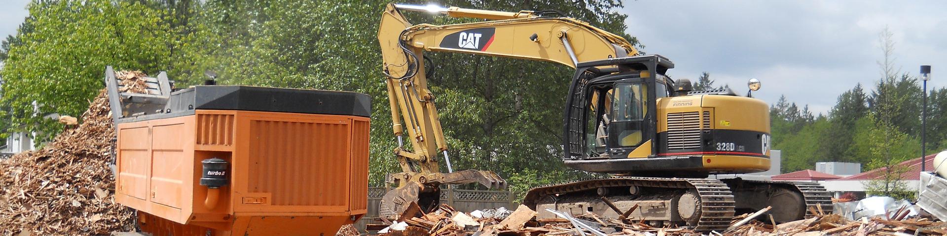 An excavator puts debris from a demolition into a wood chipping machine.
