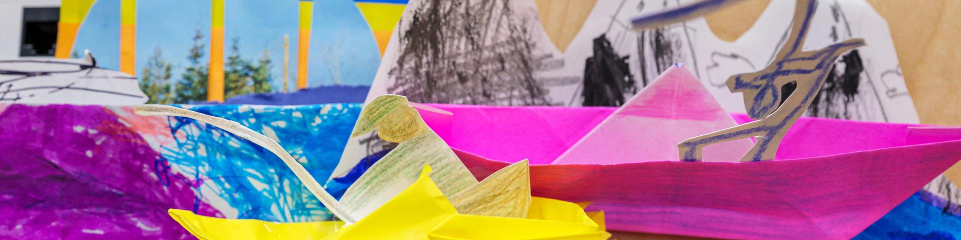 Colourful paper boats sail across the top of a collage of paper.
