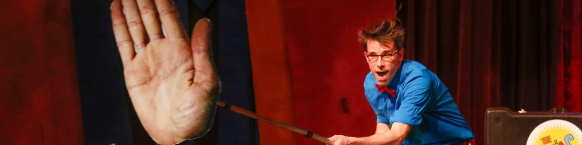 Alex Zerbe performs his Zaniac show with a giant hand cut-out on a stick displayed to the audience.