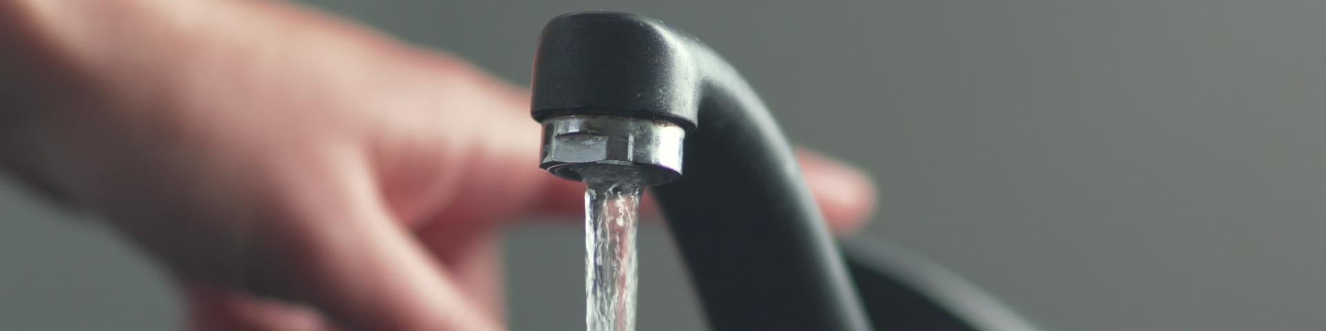 A person turns off a running tap.