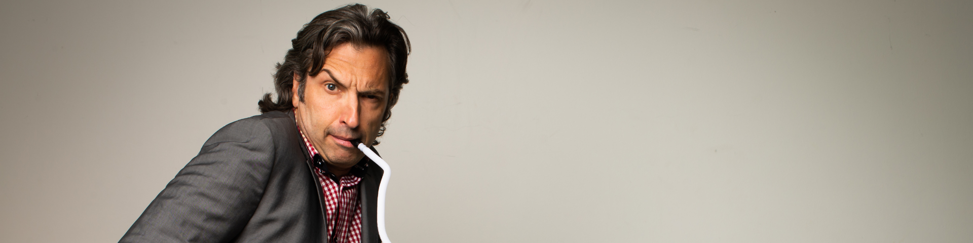 A man playing a melodica raises his eyebrow against a neutral grey background.