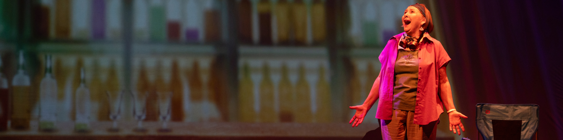 A female performer looks up while on stage, standing against the backdrop of a liquor store.