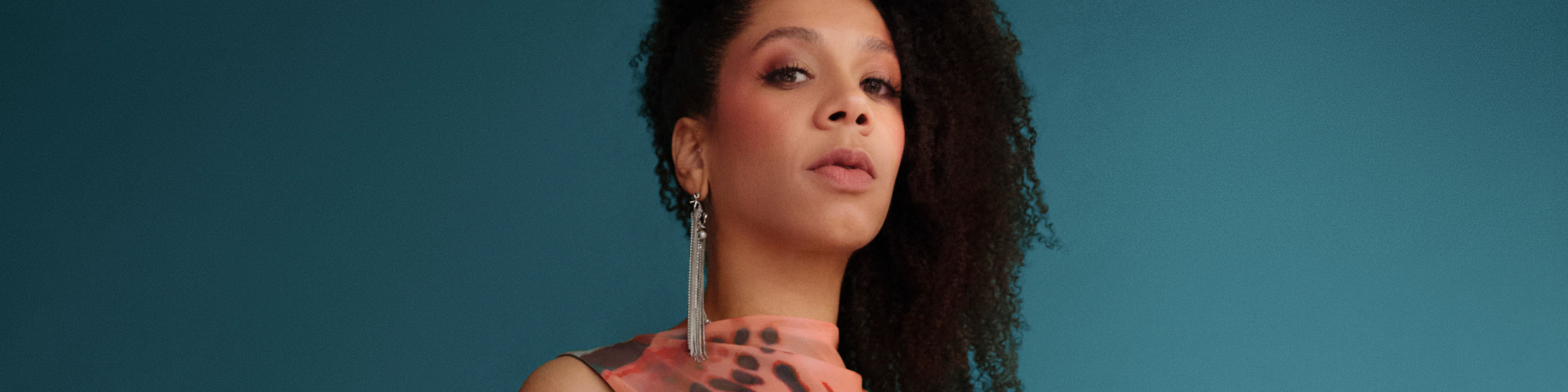 Tina Leon looks at the camera in a fancy pink dress against a blue background.