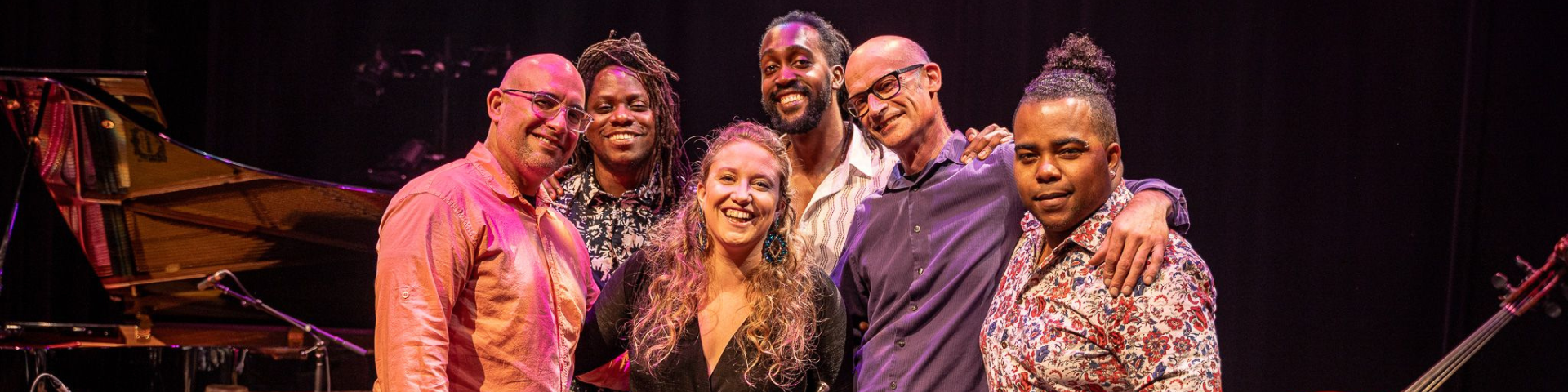 The Rachel Terrien Latin Jazz Quintet smiles for a group photo on a dark stage with a spotlight.
