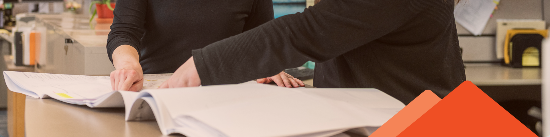 Two woman point to a single spot on a set of building plans.