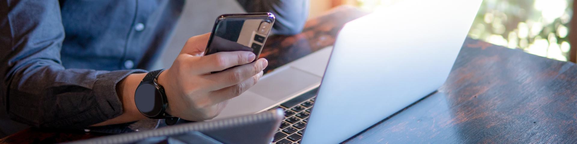 A man checks his phone while simultaneously working on a laptop and tablet.