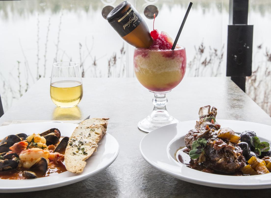 Two full plates of food sit on a table next to a window showing the scenic river below.
