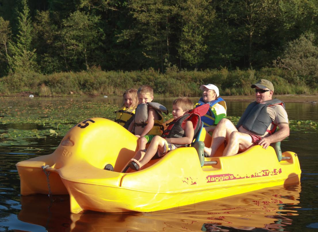 A family wearing lifejackets enjoys the water from atop a yellow paddleboat.