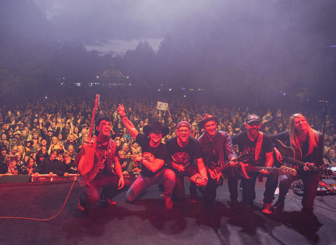 Aaron Pritchett and his bandmates pose onstage to take a "selfie" with the crowd at the 2024 Our Neck of the Woods event in Memorial Peace Park.