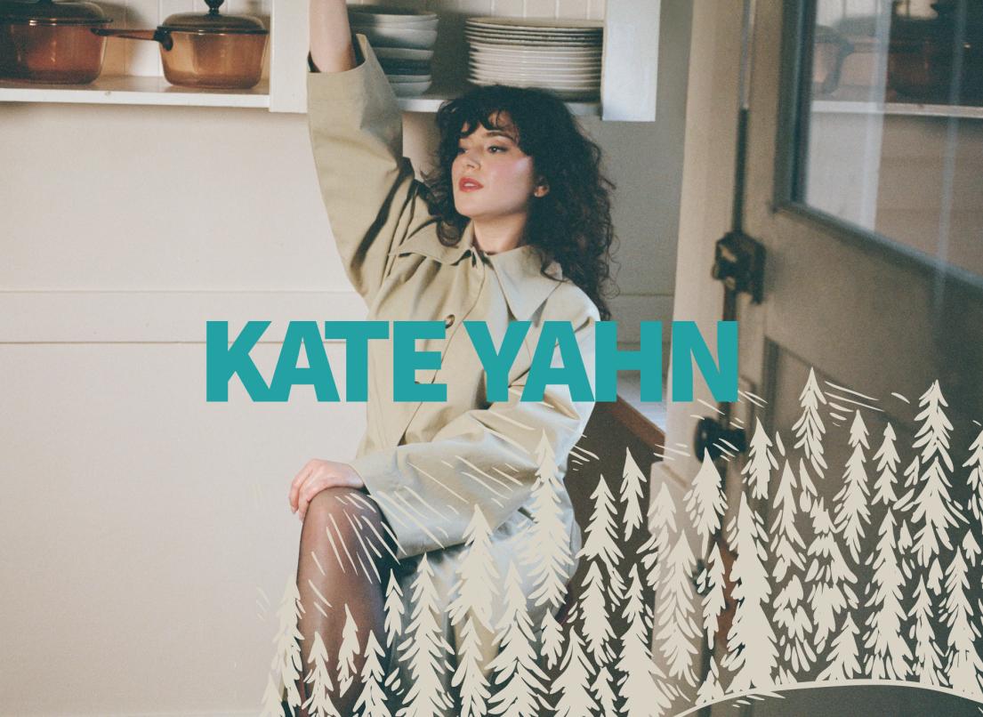 Kate Yahn sits on a chair in a kitchen next to a high counter with white plates and bronze pots.