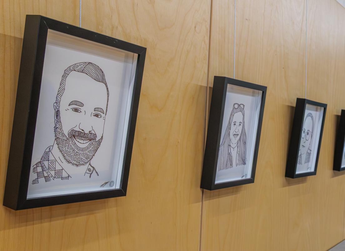 Black-and-white drawn portraits in thick black frames line a wall as part of the Constellation art display by Alex Neff.